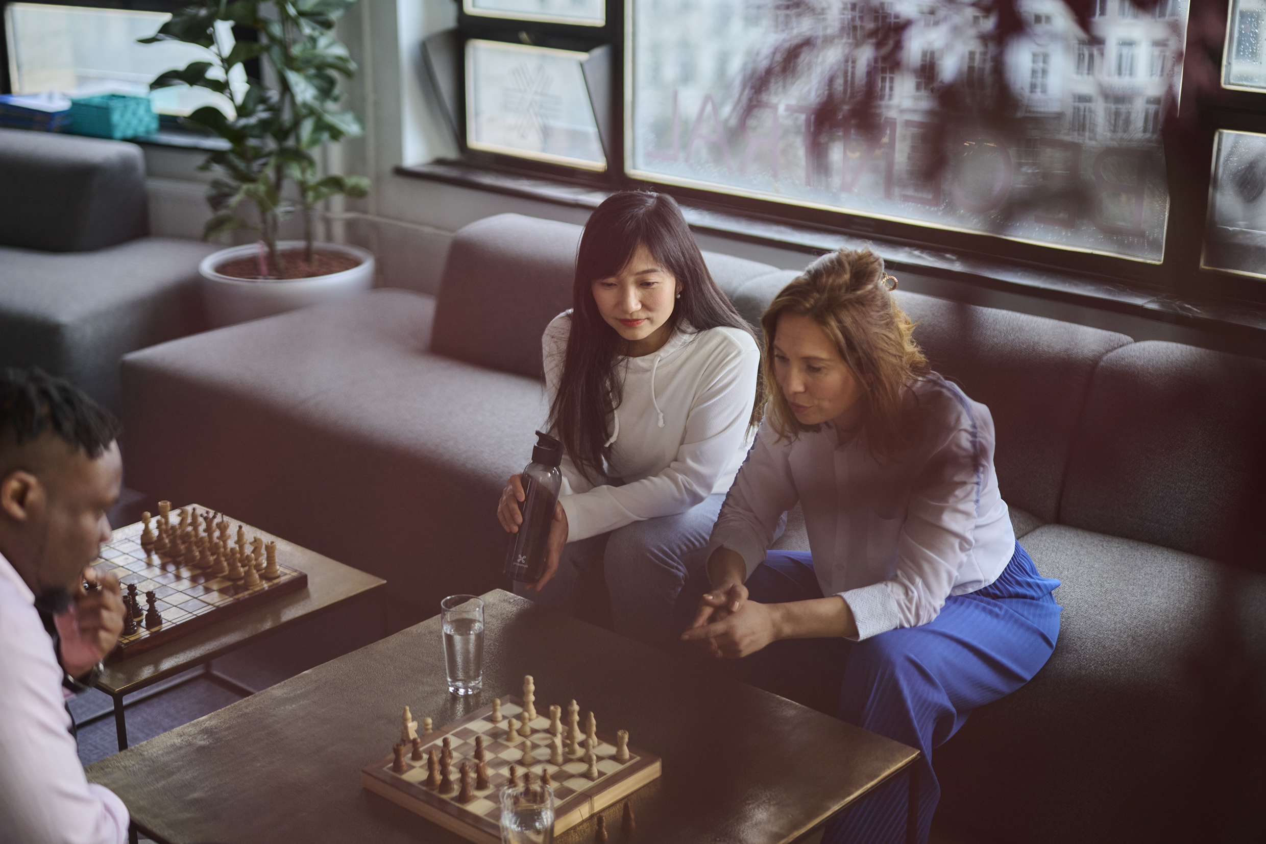 Two Woman and a Man sitting around a Chess Game Table in the Office